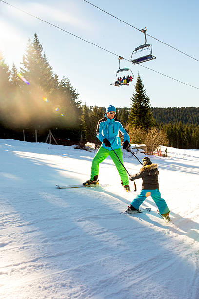 Ski instructor practicing with child on ski slope. Ski coach teaching small kid to ski on a mountain while holding for ski poles together and moving downhill. ski instructor stock pictures, royalty-free photos & images