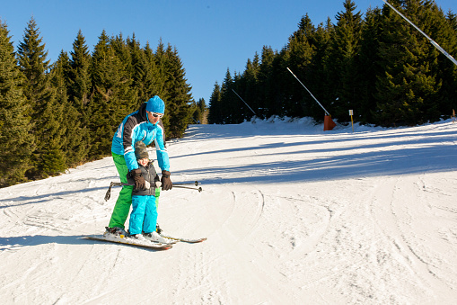 Little boy having fun during winter while skiing with coach at ski slope.