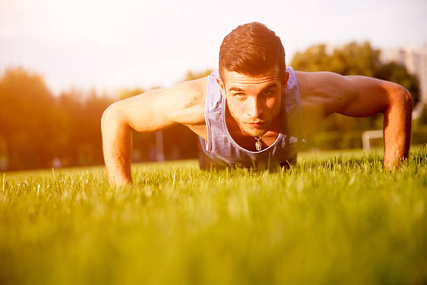 istock Young athletic guy in blue shirt press ups outdoors 615107708