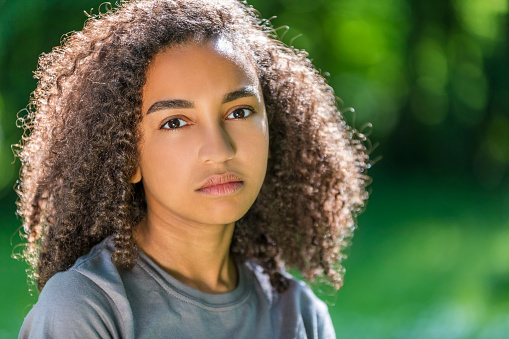 Beautiful mixed race African American girl teenager female young woman outside in spring or summer looking sad depressed or thoughtful