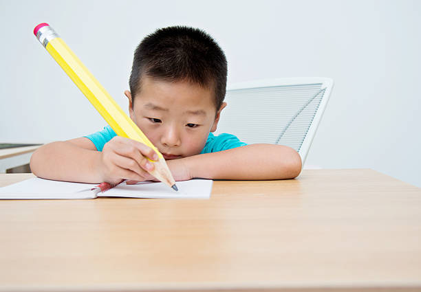 istock Little asian boy writing with a large pencil 615112562
