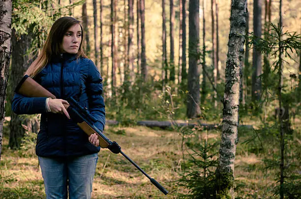 Young pretty girl with rifle in forest