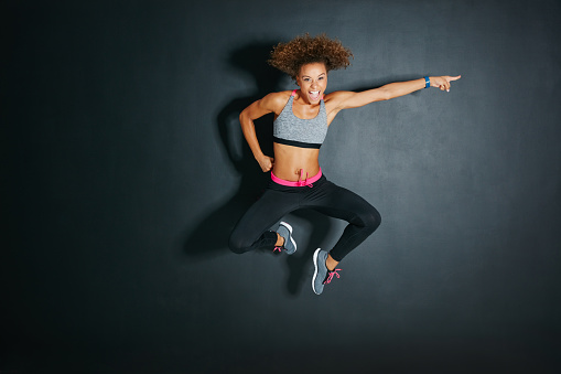 Shot of a sporty young woman jumping against a grey background