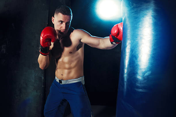 istock Male boxer boxing in punching bag with dramatic edgy lighting 615239482