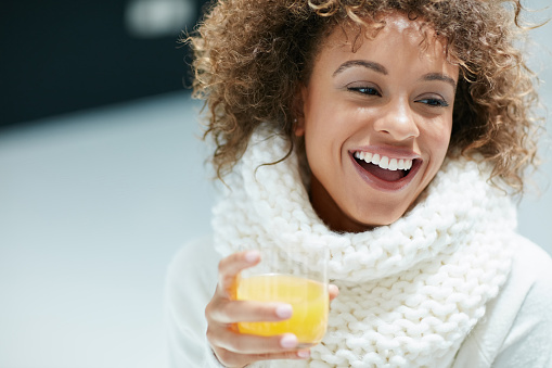 Shot of a young woman dressed in warm clothing drinking a glass of orange juice