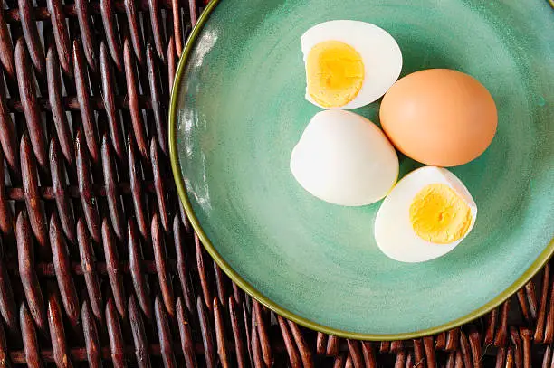 Hard-boiled egg cut and piled on egg slicer and full egg with shell on green plate or dish.