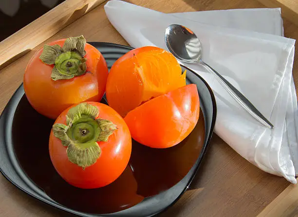 ripe tasty persimmon fruits on blue plate, closeup 
