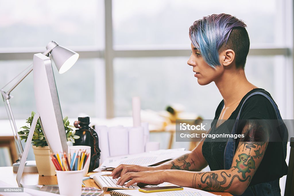 Stylish everywhere Side view of alternative style woman working on computer in office Tattoo Stock Photo