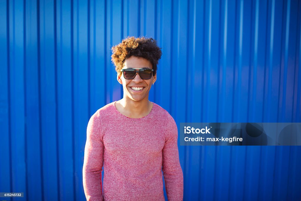 Head and shoulders portrait of young African American man young African American man over blue background wearing sunglasses. Cool teenager with stylish hairstyle smiling over color wall Men Stock Photo