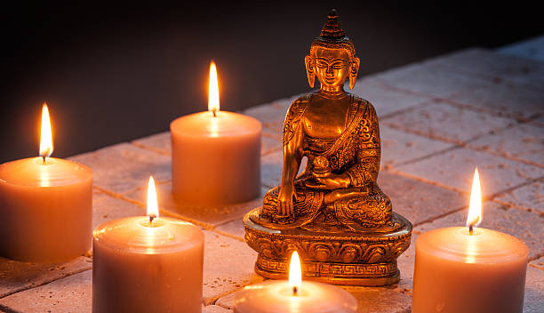 istock Bronze Buddha with warm lighted candles over limestone background 615257502