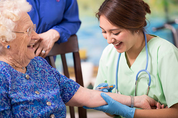 Home healthcare nurse giving injection to elderly woman. Latin descent female nurse or doctor gives vaccine, medicine, or flu shot to a senior woman patient.  Home or clinic setting.  Her daughter looks on.  Woman is over 100 years old! over 100 photos stock pictures, royalty-free photos & images