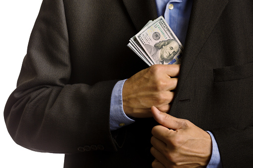 A businessman pocketing U.S. currency money, the dollar bills into his suit pocket. Concept photo of relationship between business and international trade. Photographed on white background in studio.