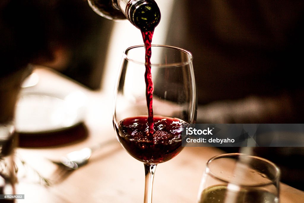 Wine Pouring into Glass Red wine being poured into a stem glass at the table. Wine Stock Photo