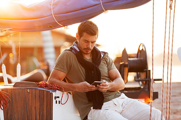 Handsome Mann mit Handy auf Segelboot im Sonnenuntergang – Foto