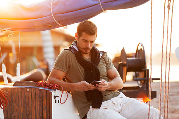 Hombre guapo usando el teléfono celular en el velero al atardecer - foto de stock