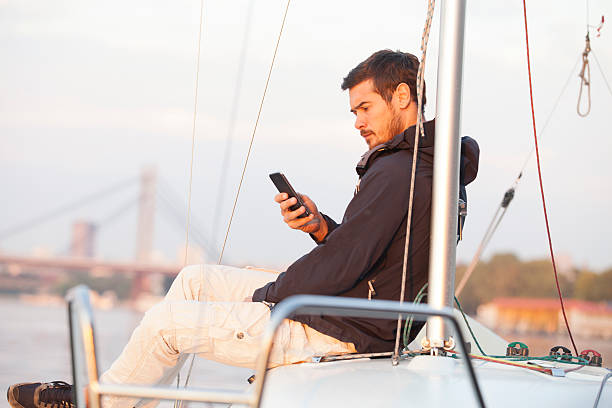 Hombre guapo usando el teléfono celular en el velero al atardecer - foto de stock