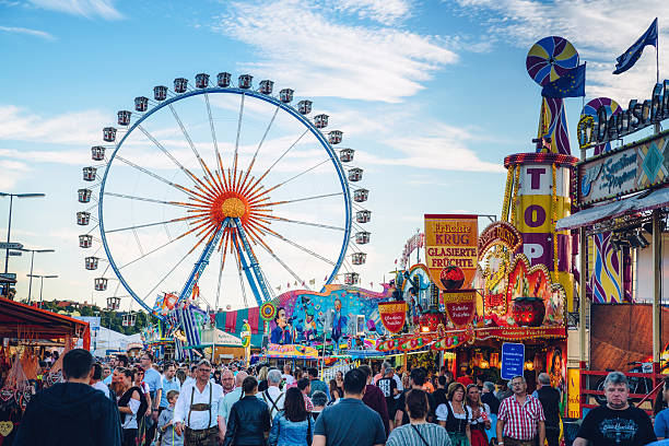 Munich, Germany - September 29, 2016:  Visitors Walking Through Oktoberfest Fairgrounds at sunset, Ferris Wheel in the background.