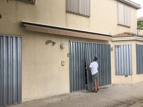 Man installing hurricane metal shutters on house door, Miramar, Florida, USA