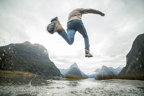 Young man hiking jumps over the mountain river. Low angle view, shot in Autumn in New Zealand.