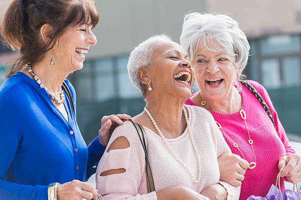 Three multi-ethnic senior women out shopping A group of three multi-ethnic senior women in their 60s and 70s standing outdoors, laughing. They are carrying shopping bags. older woman purse stock pictures, royalty-free photos & images