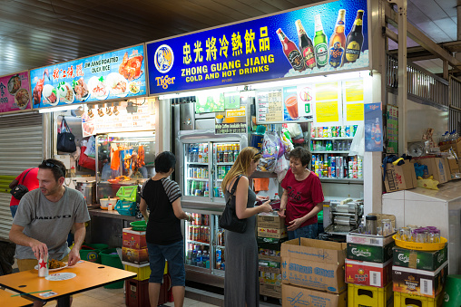 Singapore, Singapore - October 08, 2016: Owner of the drink stall selling beer to a Caucasian couple.