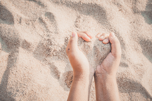 Hands of woman kids holding sandy to heart shape on beach. summer season.