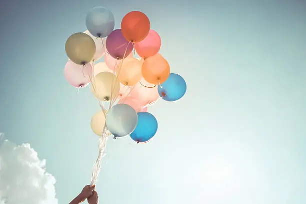 Hands of girl holding multicolored balloons done with a retro vintage filter effect, concept of happy birthday in summer and wedding honeymoon party (Vintage color tone)