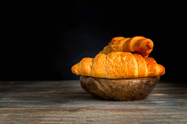 istock Fresh croissants on wooden board against black background. 615393694