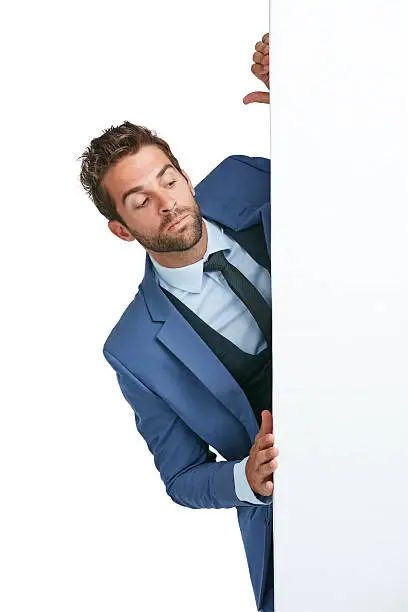 Studio shot of a handsome businessman peering around a wall against a white background