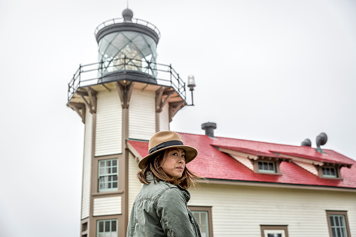 Stock photo of a woman wearing a fedora hat outside of a lighthouse on a foggy day