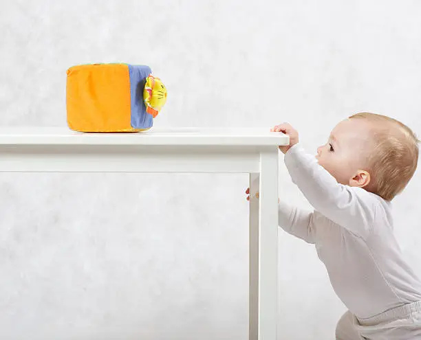 A baby of eight months old is making some activities on a gray background.