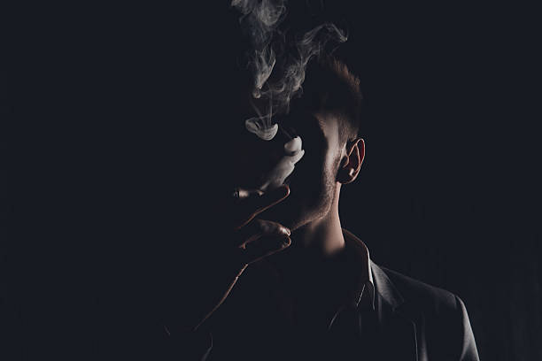 homme mystère avec cigare et fumée isolée sur fond noir - smoking issues photos et images de collection