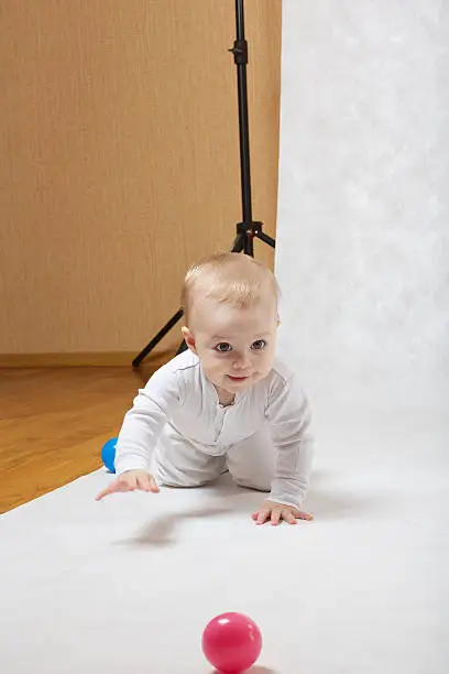 The first photo session of an eight months baby. The girl is crawling in the photo studio