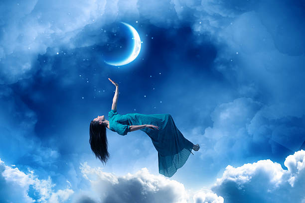 Light painting of a moon behind a young woman in a white dress standing in a field at night.
