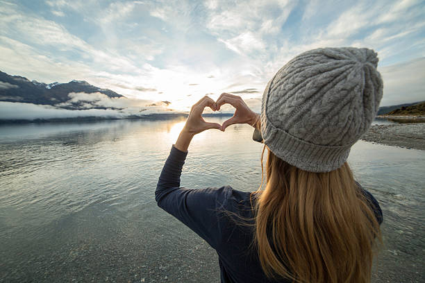 istock Young woman by the lake makes heart shape finger frame 615404582