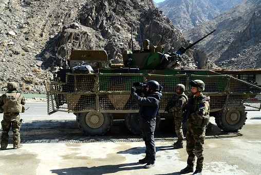 Gwan, Afghanistan - February 23, 2012: Videographer with army soldiers by armored vehicle at battlefield during a patrol. 