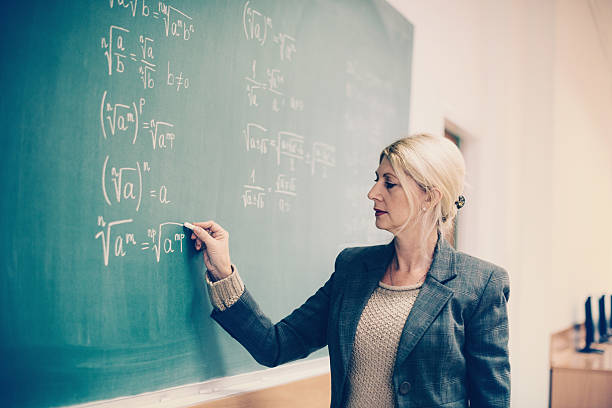 istock Mature professor in classrom writing formulas on blackboard 615411356