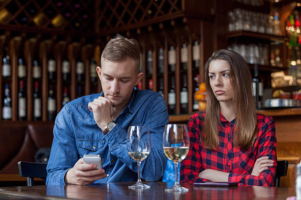 Young couple with problems Sulking woman sitting next to man reading text messages in restaurant ignoring stock pictures, royalty-free photos & images
