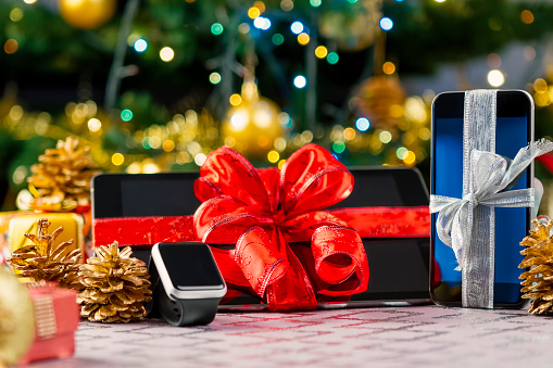 Tablet pc, smartphone and smartwatch with gifts and decorations in front of Christmas tree. Focus on smartphone.