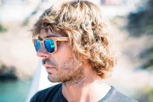 Portrait of long haired handsome man with wooden sunglasses with blue lens