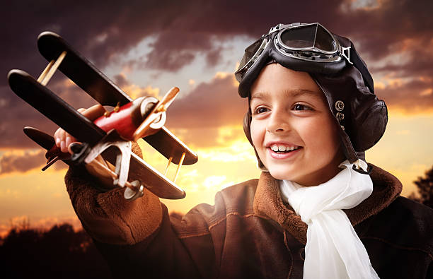 Boy playing with wooden toy airplane Boy wearing old-fashioned aviator hat, scarf and goggles holding a wooden biplane up in the air with sunset pilot photos stock pictures, royalty-free photos & images