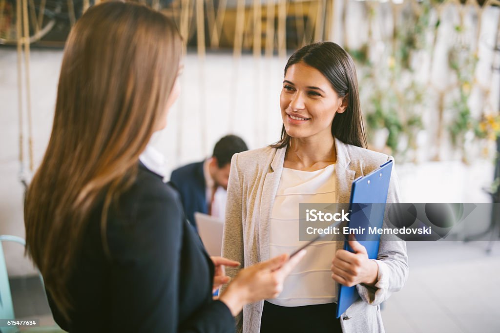 Two young businesswomen discussing business strategy using digital tablet Two young businesswomen are discussing business strategy in the office building hallway using digital tablet. Over the shoulder. Focus On Foreground Stock Photo