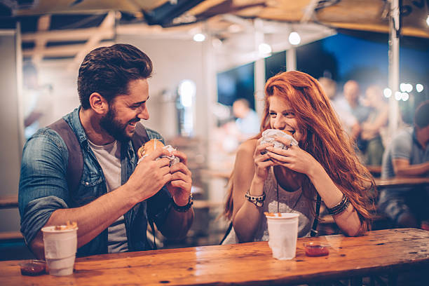 Music festival food is grate A young couple having snack and drink at an outdoors music festival. Eating burgers with fries and drinking beer. fast food restaurant photos stock pictures, royalty-free photos & images
