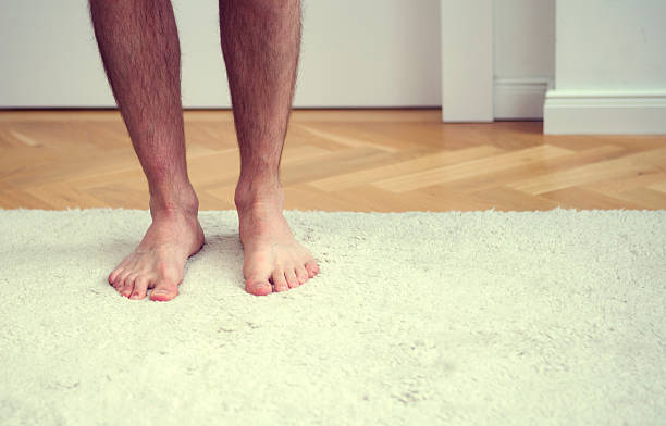 istock bare feet of man standing on white carpet 615480884