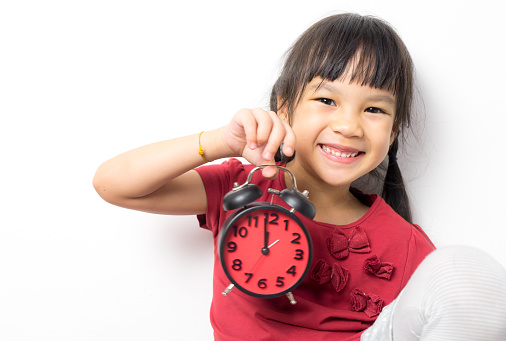 Asian girl is holding an alarm clock that count for lunch time. Little Asian girl is very happy to get a lunch break. Asian girl is smiling and holding an alarm clock counting down to 12.