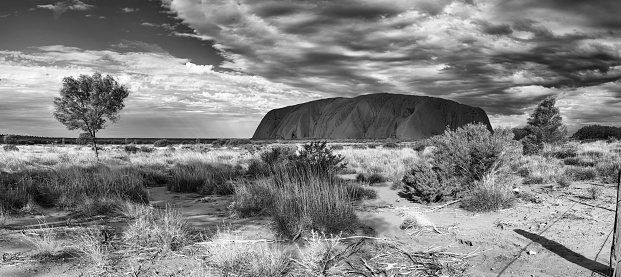 Uluru, Northern Territory, Australia - March 28, 2016: Black and white panoramic showing a bank of clouds drifting over Uluru (also known as Ayers Rock) in the Australian Outback. A genuine Wonder of the Natural World (and a UNESCO World Heritage Site), it's also a sacred place to the local Anangu people.