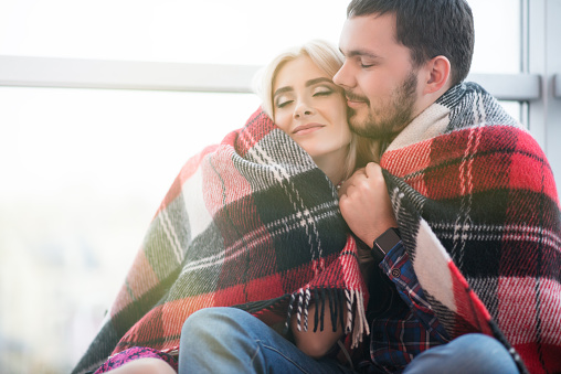 Cheerful couple relaxing under blanket at home in the living room