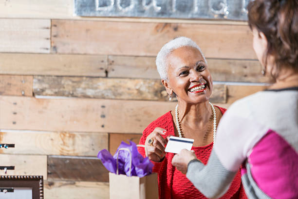 Cashier at boutique taking credit card from customer A senior African American woman working at a store at the mall, talking to customer who is paying by credit card. A shopping bag is on the checkout counter. clothing store credit card stock pictures, royalty-free photos & images