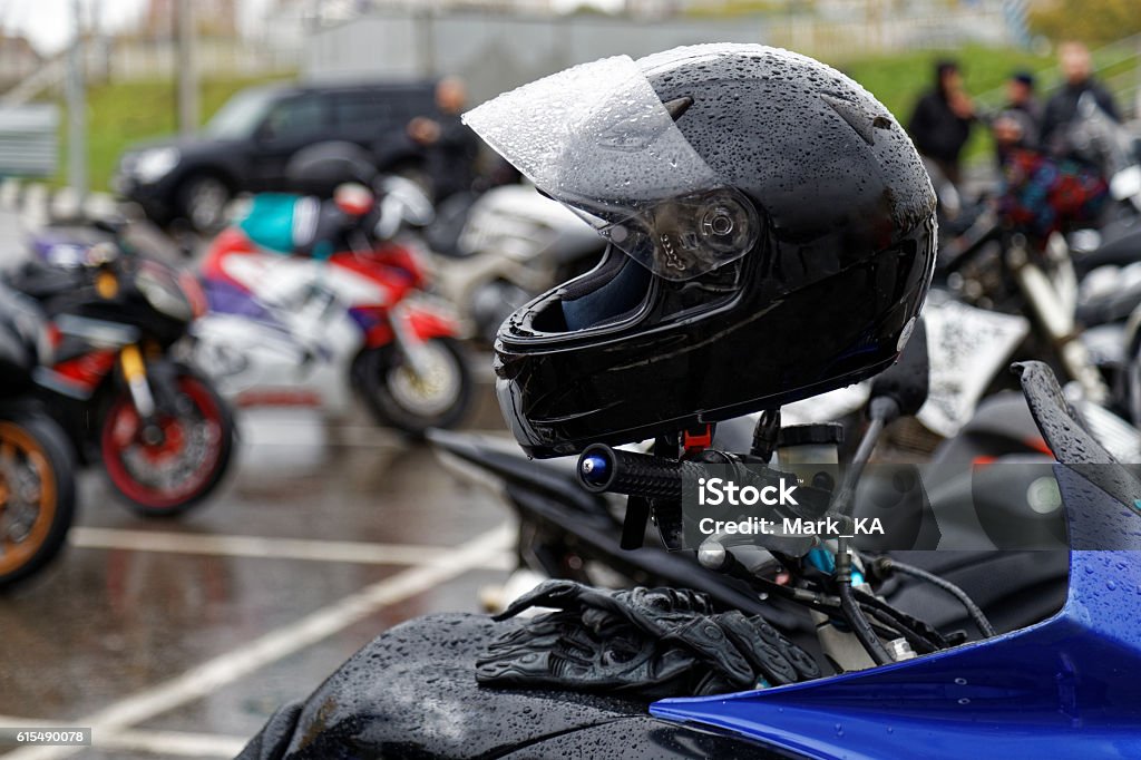 Moto helmet on motorcycle handlebars Moto helmet with drop of water on motorcycle handlebars and motorbikes on blurred background Rain Stock Photo