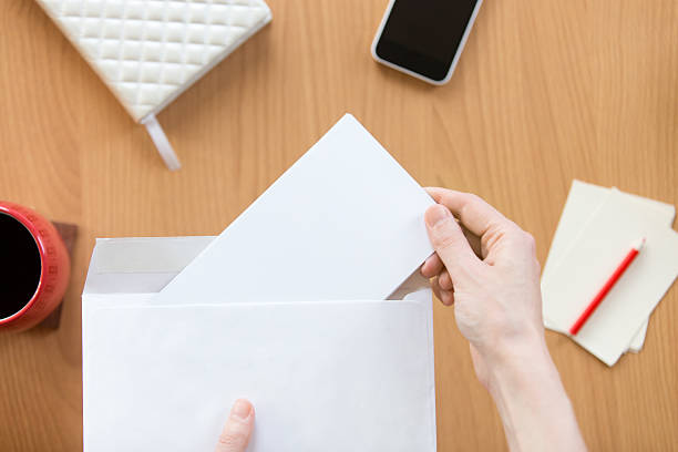 mains féminines tenant une enveloppe avec une feuille au-dessus du bureau - document reading human hand caucasian photos et images de collection